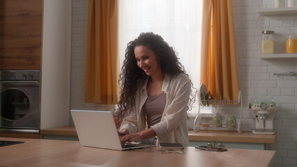 Smiling Hispanic freelance woman Latino girl female businesswoman freelancer working distant from home kitchen writing notes business work laptop computer typing shopping online using Internet app