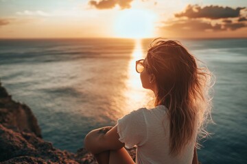 A woman sits peacefully on a cliff, watching a vibrant sunset over the ocean. The scene captures tranquility and reflection in beautiful natural light.