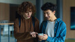 © Yuliia - Two teenagers friends Caucasian males men guys pupils students schoolboys walking going in corridor university college school boys looking in mobile phone app shocked laugh smile talking online news