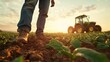 © familymedia - A farmer stands in a lush field, gazing at a tractor during a golden sunset, embodying the spirit of agriculture, hard work, and connection with the earth.