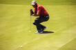 © Jacob Lund - Focused golfer aiming carefully while leaning on putter to line up a crucial shot on the green