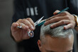 © alones - Man professional barber cuts gray hair guy with scissors and comb