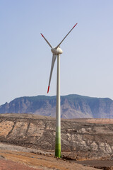 A wind turbine standing tall against a backdrop of mountains. The landscape appears calm, with the wind generator in focus, symbolizing renewable energy amidst nature.