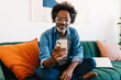 © (JLco) Julia Amaral - Man with Afro hair sitting on a couch and browsing a mobile app on his phone