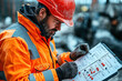 © Natalia - Construction worker in orange safety jacket and hard hat examines a checklist on a clipboard at a construction site, emphasizing safety and precision in his tasks.