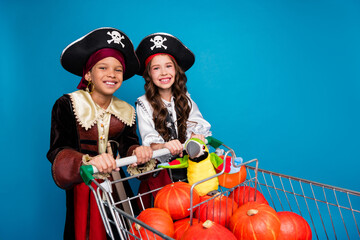 Poster - Portrait of two little kids halloween pirate costume market trolley pumpkins parrot toy isolated on blue color background