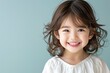 © vilaiporn - A cheerful young girl with curly hair smiles brightly against a soft blue background, radiating joy and innocence.