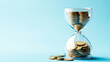 © Alina Tymofieieva - An hourglass filled with coins against a light blue background symbolizes the value of time and money in financial planning