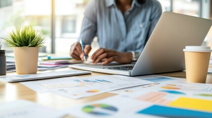 Canvas Print - A person working on a laptop at a desk surrounded by charts, plants, and coffee cups.