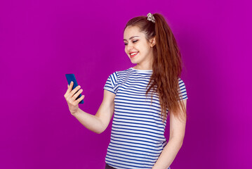 Beautiful Young Woman Making a Video Call on Smartphone, Sharing Exciting News with Friends or Family. Standing against a bright colorful background