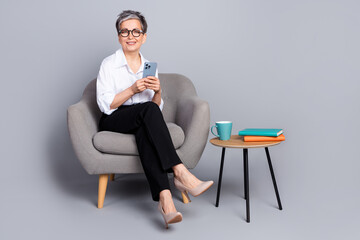 Sticker - Full length photo of lovely senior lady sit armchair hold device dressed stylish formalwear isolated on gray color background