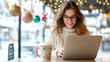 © Teeradej - Woman in cozy sweater enjoys working on her laptop in festive cafe, surrounded by holiday decorations and warm lights.