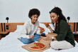 © Bliss - Two women share laughs and pizza in their cozy hotel room, capturing moments of love and adventure.