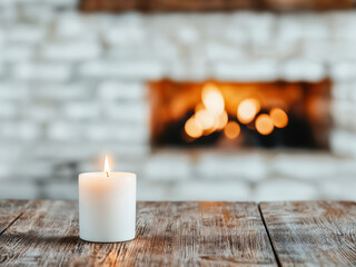 Aufkleber - White candle burning on an empty wooden table with a fireplace in the background, creating a cozy and inviting atmosphere