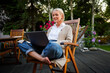 © baranq - Mature woman outdoors using laptop in backyard patio