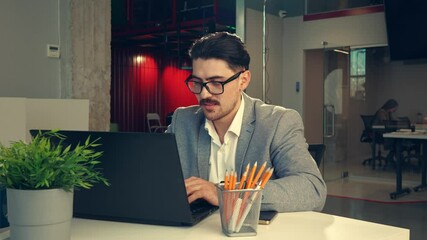 Poster - young professional working intently on a laptop in a modern office environment during daylight hours