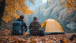 © SmirkDingo - Couple camping in autumn, sitting near a tent with backpacks by a scenic lake, enjoying the peaceful nature.