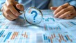 © TA Design - A person examining data on a document with a magnifying glass, highlighting a question mark, indicating inquiry or research.