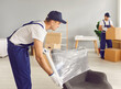 © Studio Romantic - Professional delivery and moving service. Loader wraps chair with transparent stretch film while completing order at moving service. Young man in overalls uses plastic wrap to transport furniture.