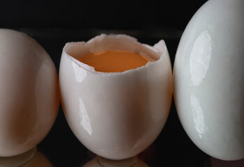 Three raw duck eggs are sitting in a row with an egg in the middle broken in half showing the yolk and white egg on dark background. use it as your Wallpaper, Poster and Space for text,Selective focus