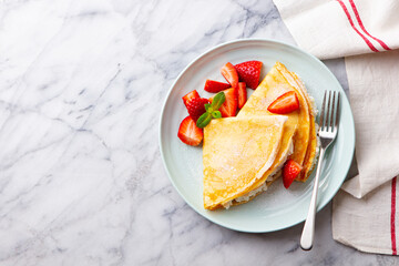 Wall Mural - Crepes, thin pancakes with cream cheese, ricotta, fresh strawberries and sugar powder. Marble background. Top view.
