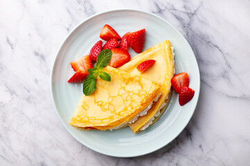 Wall Mural - Crepes, thin pancakes with cream cheese, ricotta and fresh strawberries. Marble background. Top view.