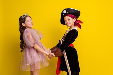 Poster - Profile photo of two kids halloween princess pirate costume hold arms empty space isolated on yellow color background