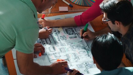 Top view of civil engineer team writing at blueprint at meeting table with color palettes. Group of smart diverse people planning and taking a note while manager looking at project plans. Symposium.