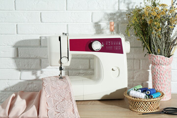 Canvas Print - Sewing machine with fabric, flowers in vase and tools on wooden table indoors