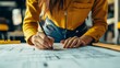 © Adi - Close up of woman architect taking notes on blueprints plans to design building layout. Engineer planning urban construction project and structure to work on architectural development