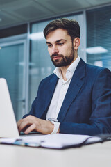 Fototapete - Concentrated male lawyer in formal wear booking tickets on website while using modern laptop device with wireless internet connection in conference room, concept of business people and technology