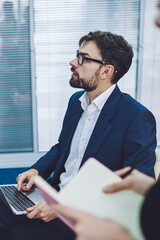 Concentrated male employer dressed in formal wear looking on flip chart and analyzing information during working process with colleague in conference room,concept of collaboration and entrepreneurship