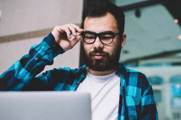 Concentrated male graphic designer using application for job on laptop computer working on freelance, man in eyewear studying online downloading files from networks on netbook via modern netbook