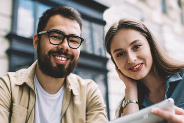 Portrait of cheerful multicultural friends smiling at camera while waiting for email via application on modern touch pad, happy couple in love enjoying time for each other, concept of relationship