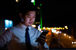 © sorapop - Stylish man holding phone in vibrant city night. Engaged in social media texting online shopping. Modern communication success businessman's urban lifestyle.