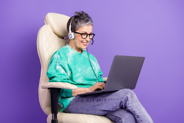 Poster - Photo portrait of pretty retired female sit armchair netbook call center wear trendy green outfit isolated on violet color background