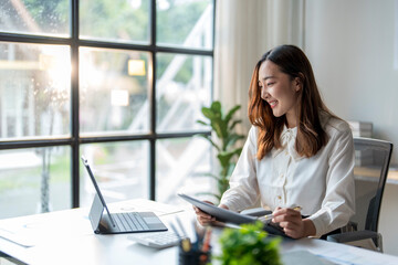 Wall Mural - young asian businesswoman smiling and working on digital tablet at office desk