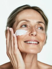 Happy middle aged 40 years old woman applying facial anti age skincare cream on face isolated on white background.