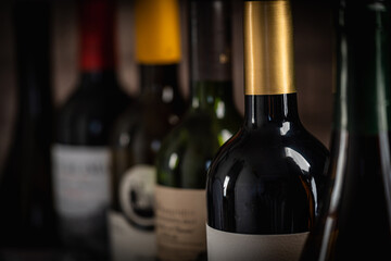 Close-up view of various wine bottles, with a glass of red wine and grapes blurred in the background, creating an elegant and sophisticated wine composition Perfect for wine-themed compositions