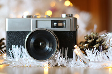 Old gray and black analog photo camera. With Christmas decoration, white garlands and white Christmas lights, out of focus. A pinecone with Christmas glitter on one side