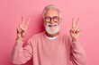 © Anna - Elderly man in pink sweater smiling and gesturing peace signs against pink background