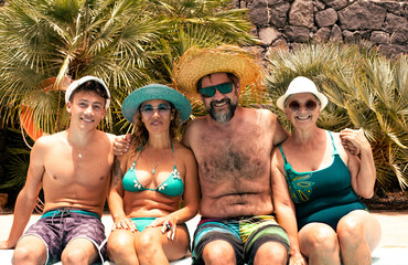 Happy multi generation family having fun together in swimming pool in a sunny summer day. Mature couple with teenage son and grandmother enjoying relax and holidays