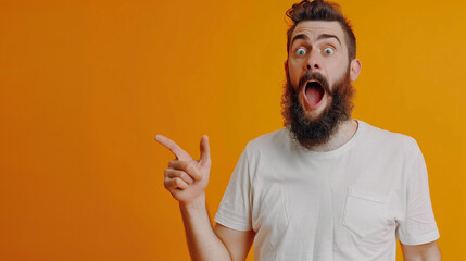 Wall Mural - Portrait of astonished young bearded man wearing white t-shirt standing with open mouth pointing away at advertisement area, copy space, close-up, isolated on orange background