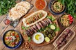 © typepng - Overhead view of grilled lamb kebabs, chicken skewers with roasted vegetables and a variety of appetizers served on a wooden outdoor table in a traditional Middle Eastern, Arab or Mediterranean