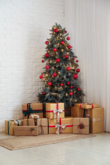 Wall Mural - Decorated Christmas tree with balls, glowing lights and gift boxes near white brick wall