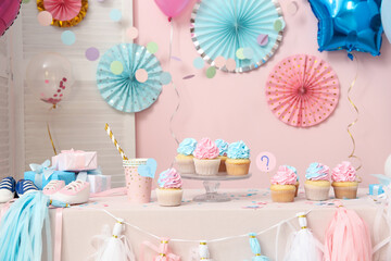 Wall Mural - Delicious cupcakes with baby booties and decorations on table against pink background. Gender reveal party concept