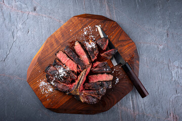 Traditional barbecue dry aged wagyu porterhouse beef steak bistecca alla Fiorentina sliced with salt and pepper served as top view on a wooden design board with a Japanese knife