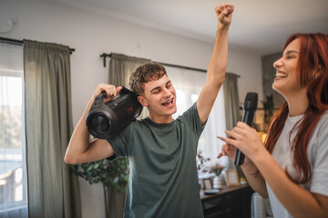 Young adult couple have karaoke night at home dance and sing together