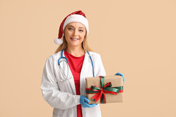 Wall Mural - Mature female doctor in Santa hat with Christmas gift box on beige background