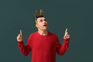 Canvas Print - Young man in reindeer horns pointing at something on green background